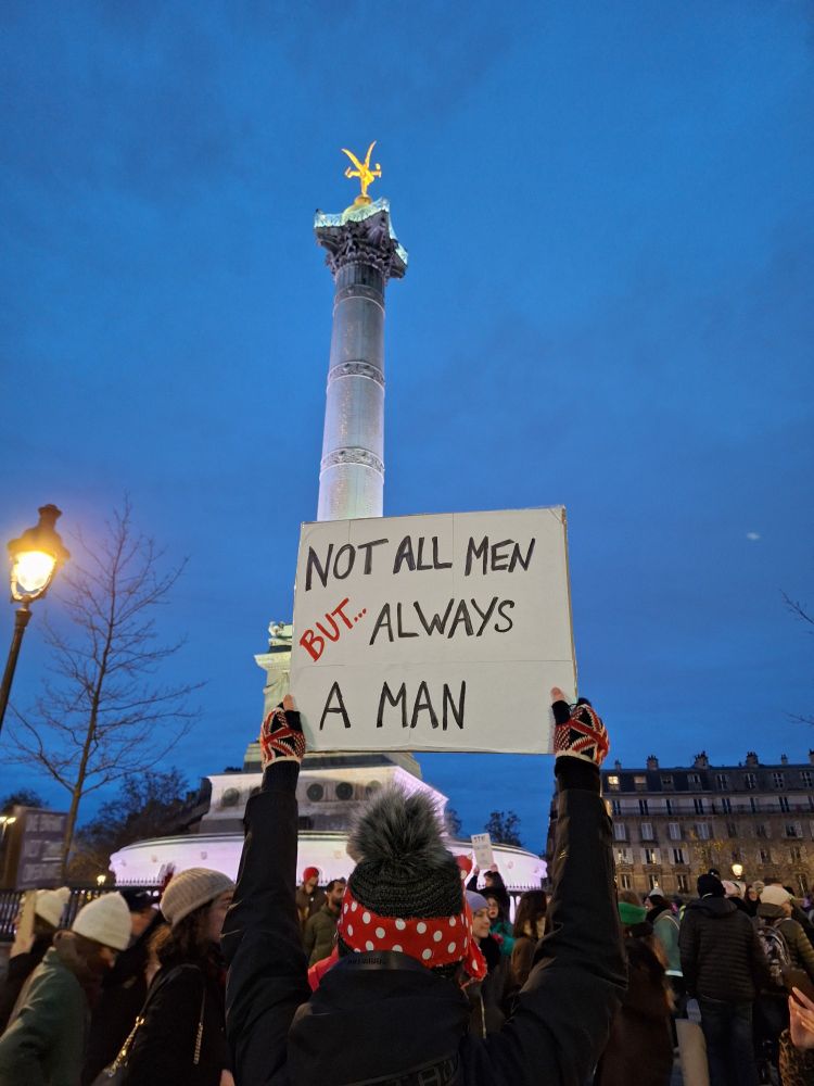 Manif NousToutes. Pancarte NOT ALL MEN BUT ALWAYS A MAN brandie face au Génie de la Bastille
