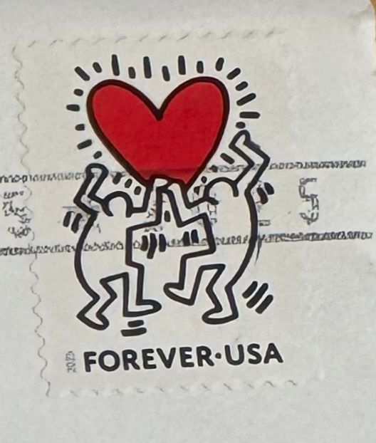 Canceled US Forever stamp with a Keith Haring drawing of two characters holding up a large red heart. 