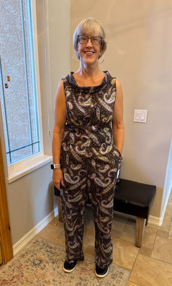 Woman standing in an entryway next to a window wearing a two piece outfit made from black-background with purple and blue paisley fabric.