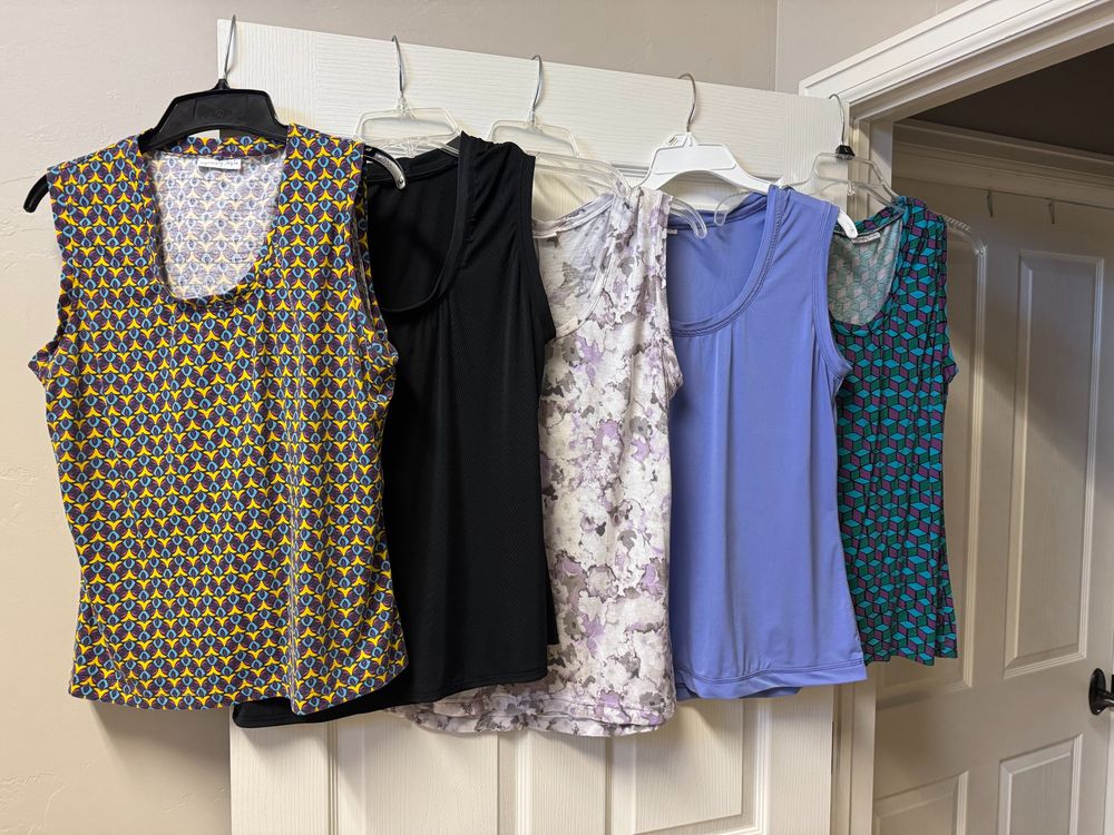 five tank tops hanging on a door.  two are solid color, 3 are patterns that include purple.