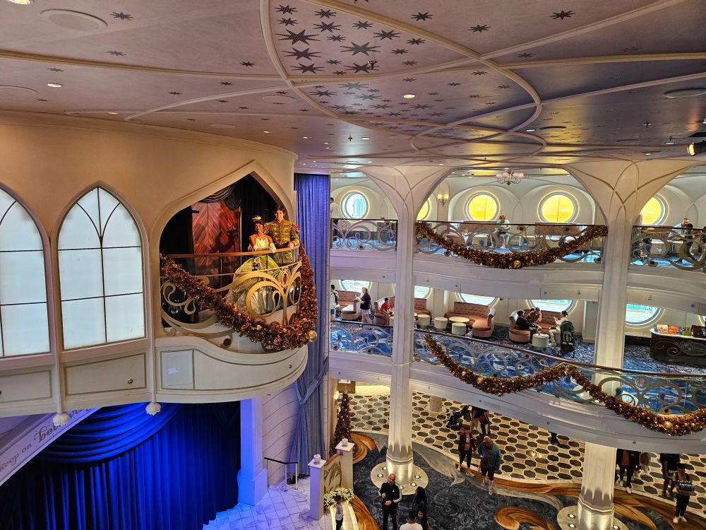 Princess Tiana and Prince Naveen in the balcony above the atrium stage on the Disney Wish.  Both are turned to face the camera.