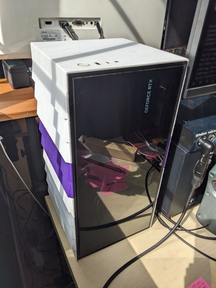 Different view of the same case with its white and purple color scheme. From this angle the front, left side, and top of the case can be seen. The power button, USB ports, and audio jack have been relocated from their original position on the right to a mirrored position on the left. 

The reflection in the glass front now reveals a slightly cluttered desk and the wooden train whistle that Niko uses to greet new followers on his Twitch streams.