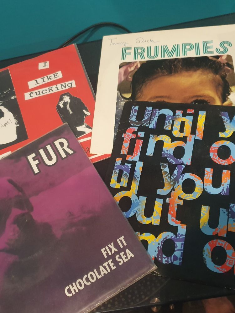 4 7" singles laid on a surface. They are Bikini Kill I like fucking, Frumpies Tommy Spicy, Neds Atomic Dustbin Until YOU find Out and Fur Fix It
