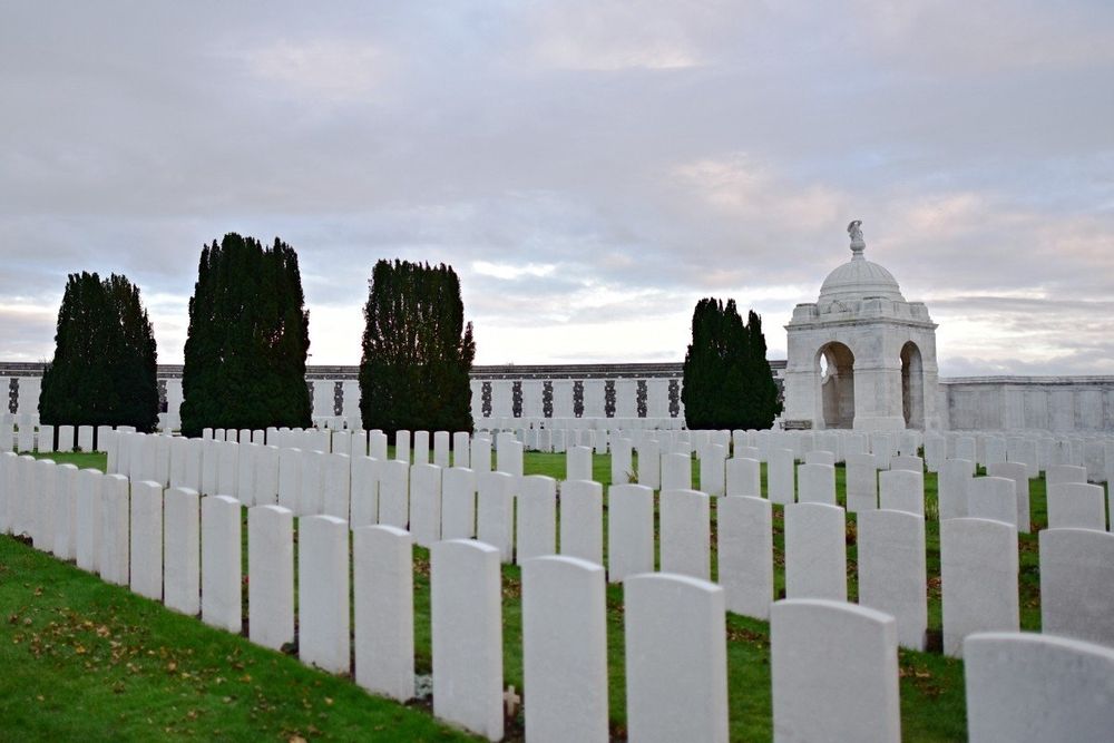 rows of identical white tombstones, 4 trees and the Memorial of the Missing wall in the background