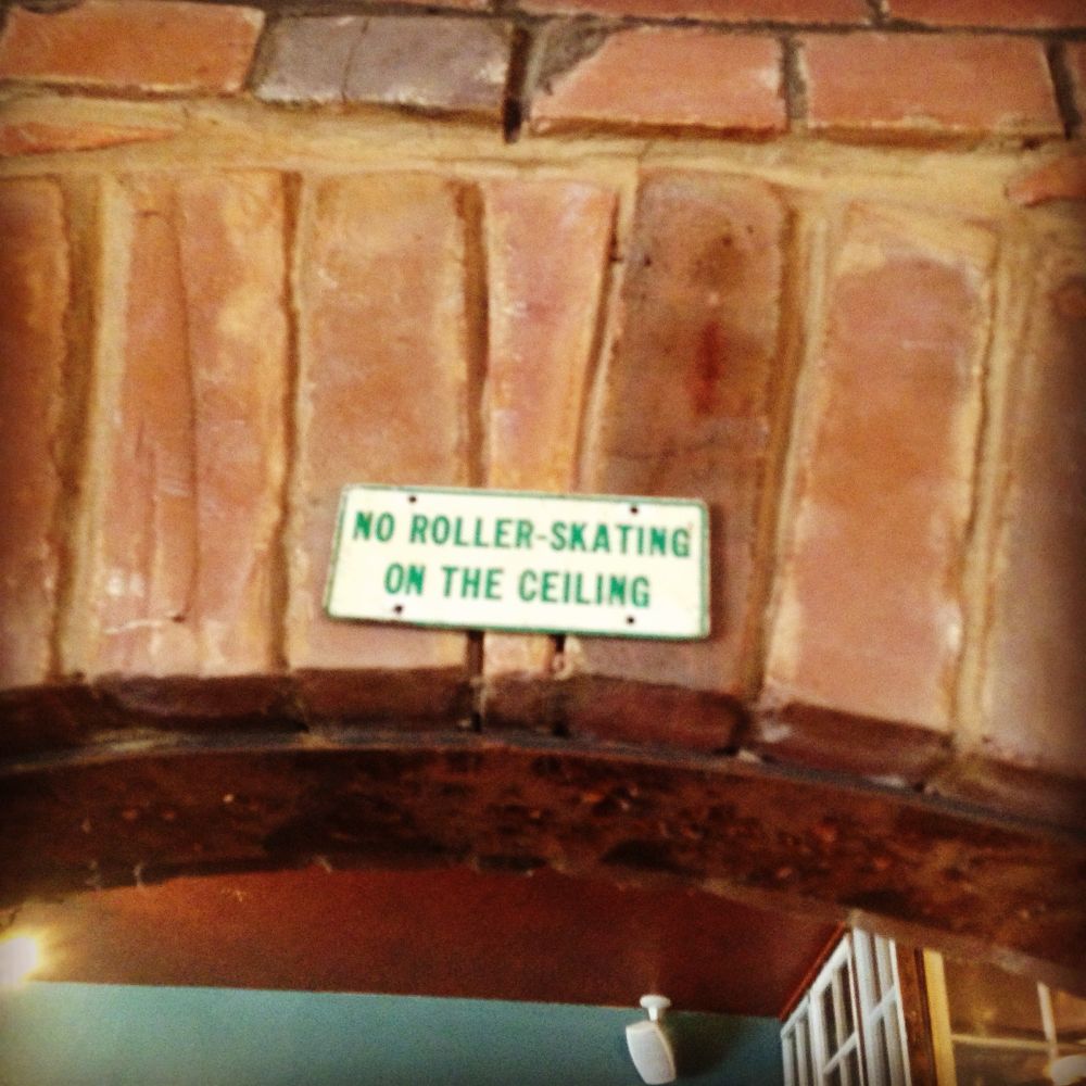 A sign above an arched doorway that says “No roller skating on the ceiling”