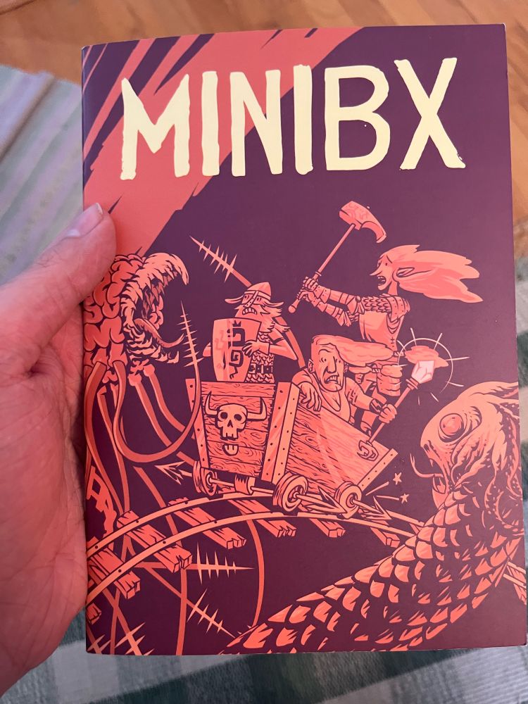 The cover of mini bx, depicting a party of alarmed adventures in a cartoony style on a minecart, whizzing past a basilisk and I think a grell? Whatever the floating brain with a beak and tentacles is called.
