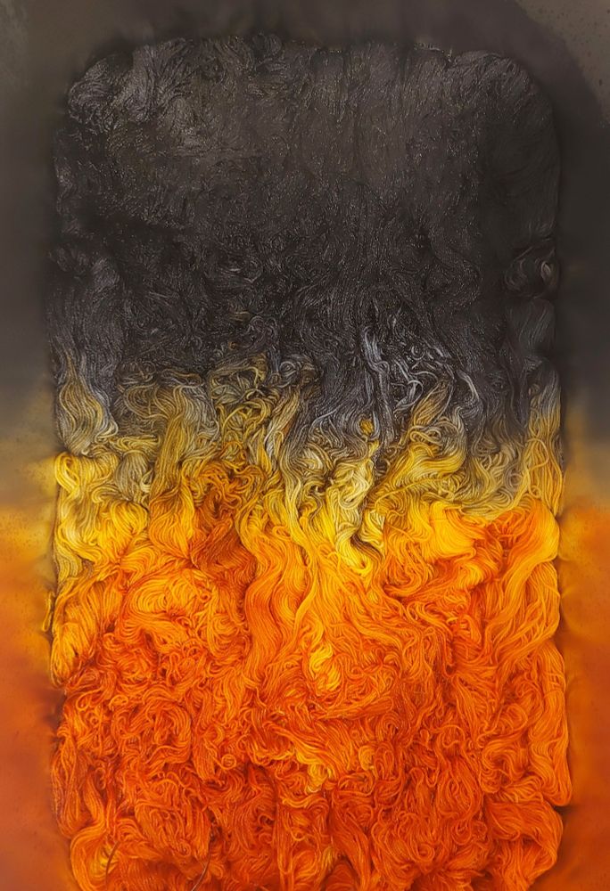 An image of yarn in a long pan. The top is black and it fades into a smokey yellow and then deep orange at the bottom. The colorway looks like a fiery image.