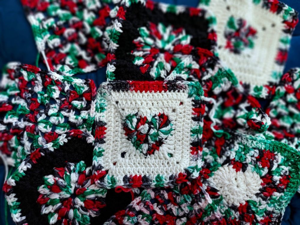 a number of granny squares with the colors of Palestine. The center granny square has a heart in it. 