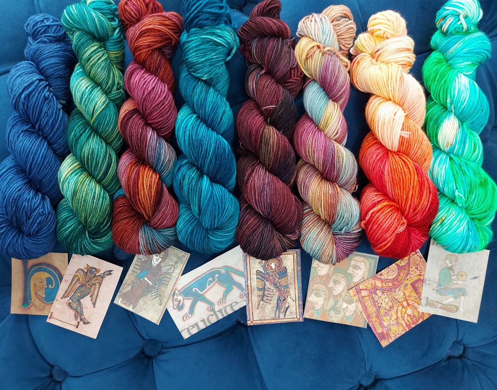 Images from the book of Kells below a row of skeins of yarn with coloe3ayd that are coordinated to match the colors in the manuscript images 