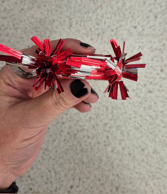My hand holding a bar magnet. Attached to the magnet are red and silver pieces of twist tie, which have formed a very beautiful pattern showing the magnetic field around the magnet.