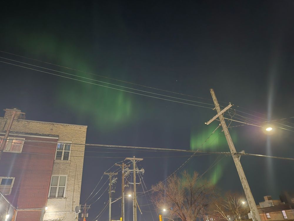 A photograph of a city skyline with green waves of the northern lights in the sky
