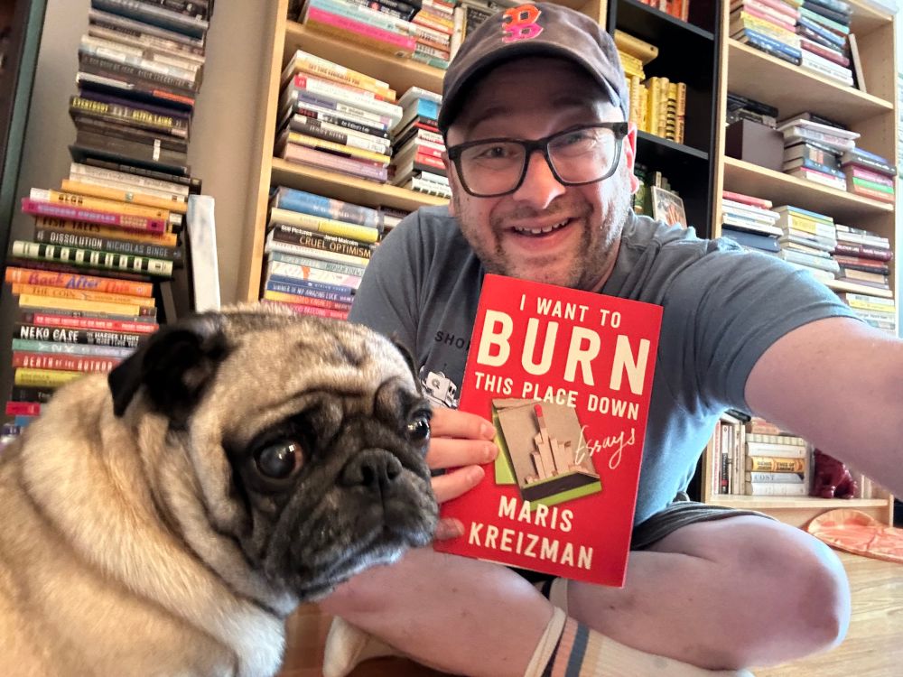 Me and Maggie the pug sitting on the floor in front of Maris’s book shelves. I’m holding a copy of Maris’s new book I Want To Burn This Place Down.
