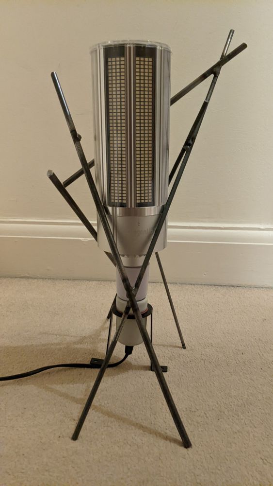 an LED corn bulb standing vertically on a beige carpet, supported by an irregular stand made out of steel rods