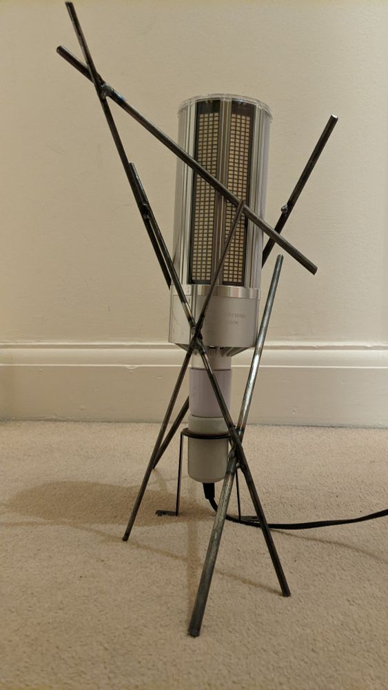 a corn bulb standing vertically on a beige carpet, supported by an irregular stand made out of steel rods