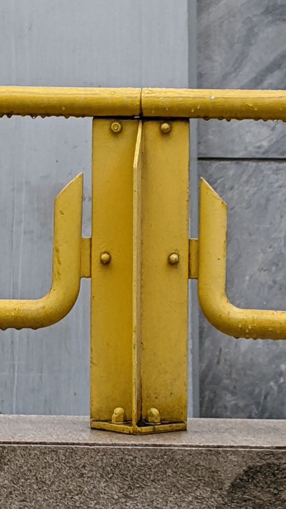 a yellow railing on a warm-toned stone base, seen against a cooler-toned grey marble wall.