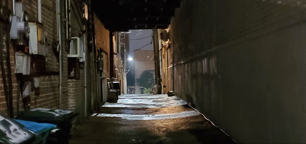 A haunted alleyway at night with a realistic ghost in center frame, unfortunately not visible due to real ghosts not being visible. There is a speck of dust that is reflecting some light that you can say is an "orb" or something if it makes you feel better though, I guess. I'm not going to say where it is, just trust me. It's there. Probably. 