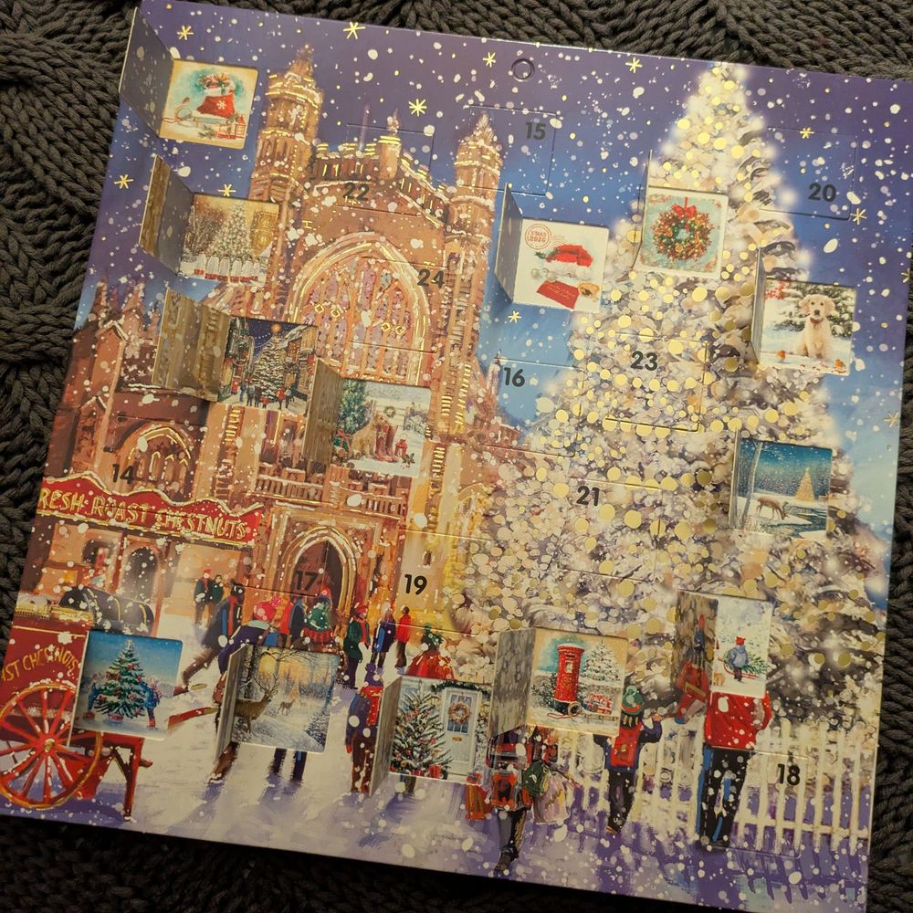 An advent calendar with a wintery scene in front of a building resembling King's College Cambridge. There's a Christmas tree, people, a chestnut stand, lots of snow and gold accents. About half the doors are open, revealing AI generated Christmas scenes with no coherent art style 