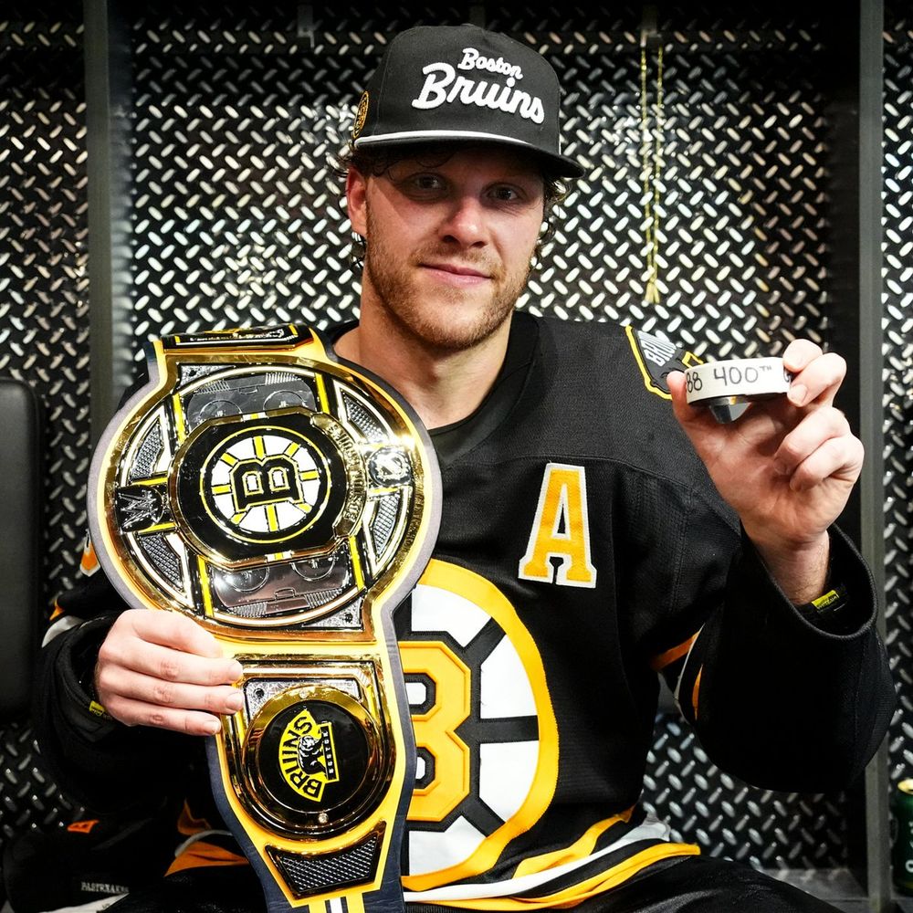 David Pastrnak holds up his 400 goal puck and the postgame player prize belt
