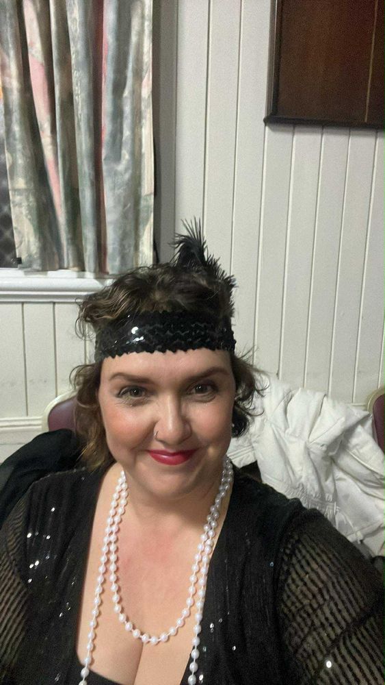 Lady wearing a black Gatsby headband and  a long pearl necklace. 