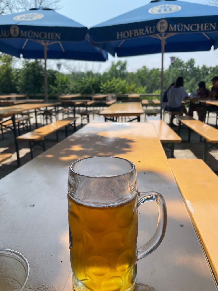 A half liter of beer in a dimpled glass on a tae outside at a beer garden because I am a brave little boy for sitting in that cold dealership for an hour. 
