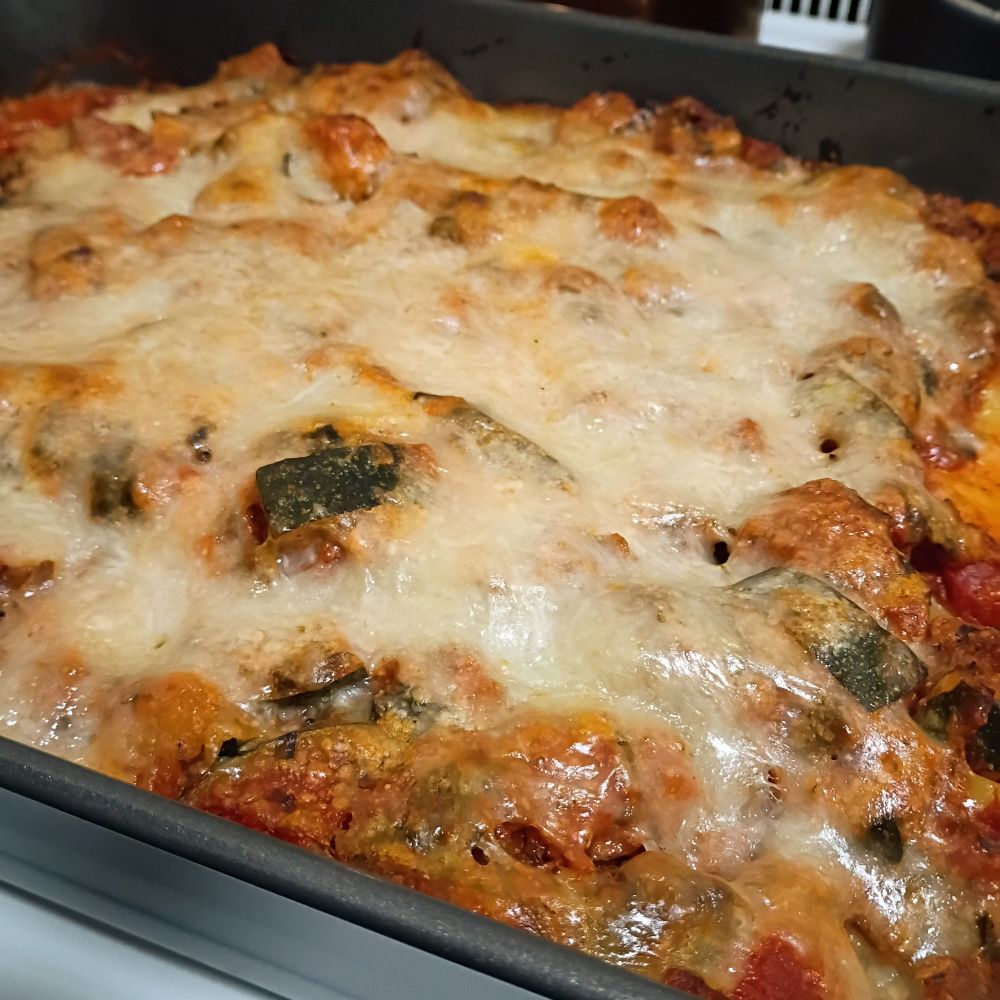 lasagna still in the pan, uncut. zucchini peeks through a layer of melted and lightly browned mozzarella. 