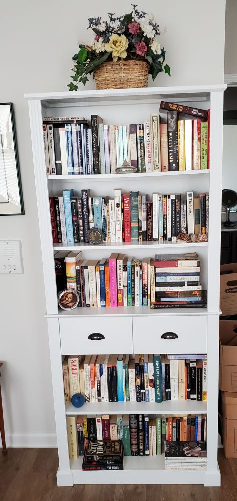 White bookshelves with two drawers, and fiction books listed by author from J-Y.
