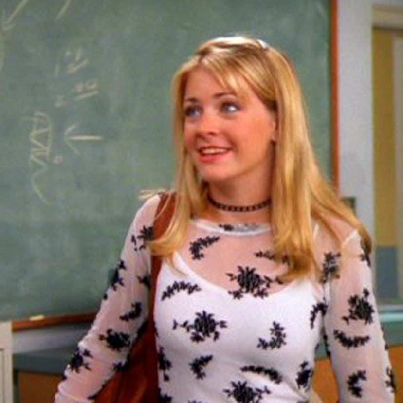 Sabrina the teenage witch wearing a see through top with a white tank top under it, long blonde hair, and a plastic choker. She's in front of a classroom chalkboard. The 90s!