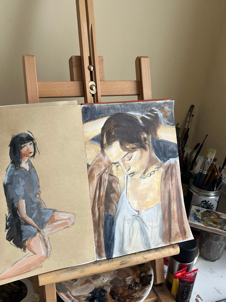 A couple of poor looking paintings on a desk easel, surrounded by brushes and assorted materials