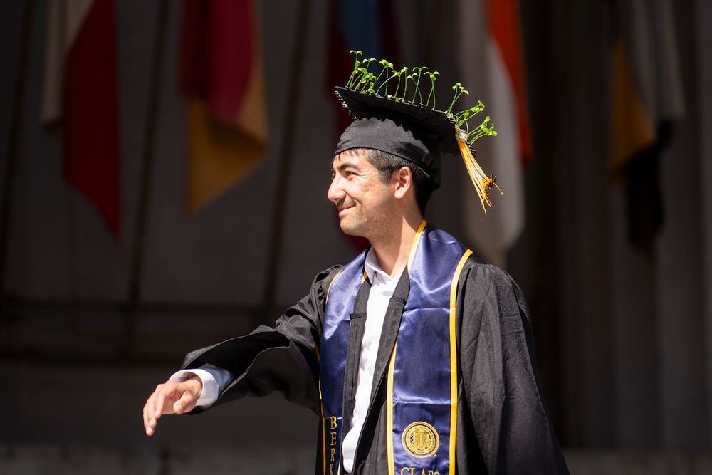 Graduate in academic regalia smiles while walking at commencement, sprouts decorated on a mortarboard. (Photo by Adam Lau / Berkeley Engineering)