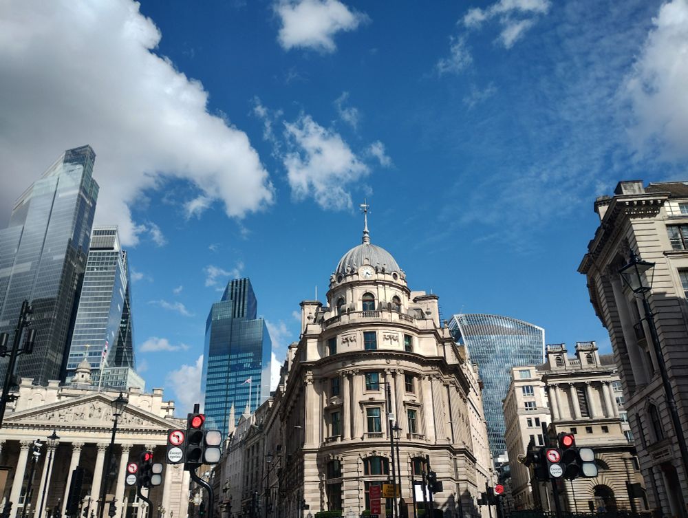City of London buildings (including the Royal Exchange) against a blue sky.