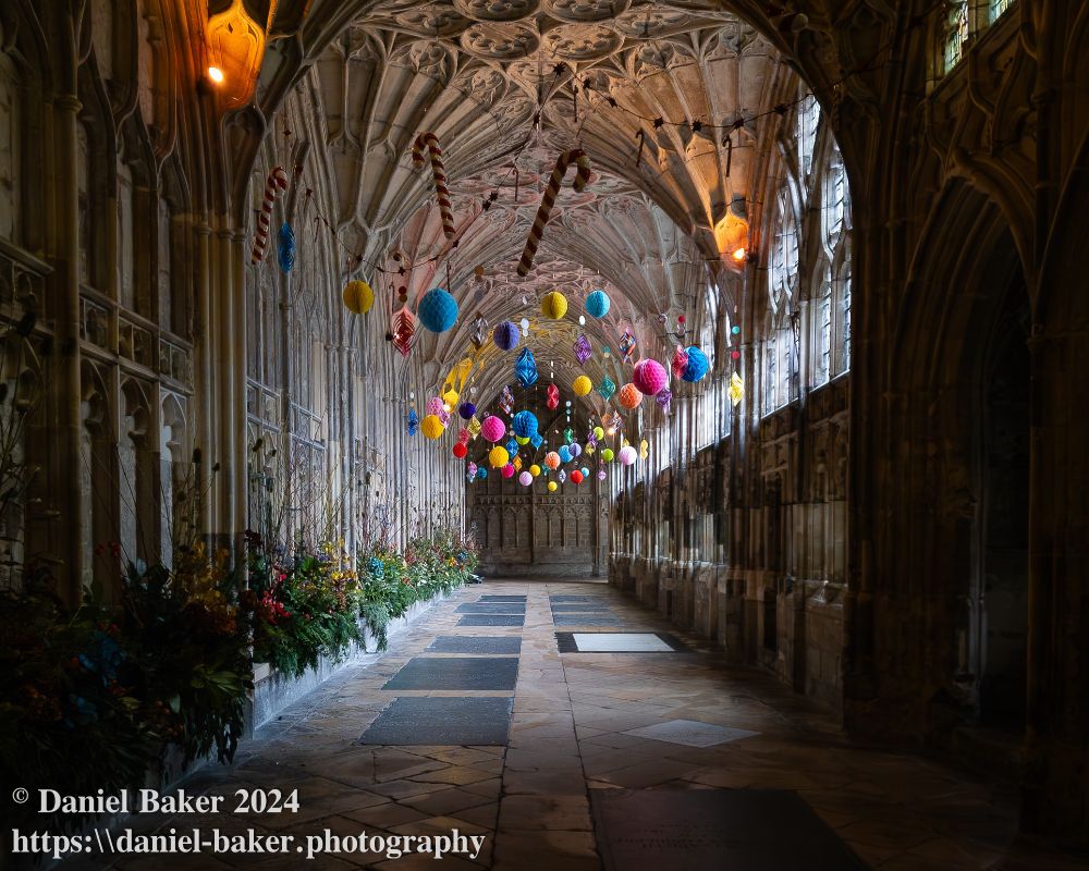 photo of the cloisters at Gloucester cathedral with colourful Christmas decorations hanging from the ceiling 