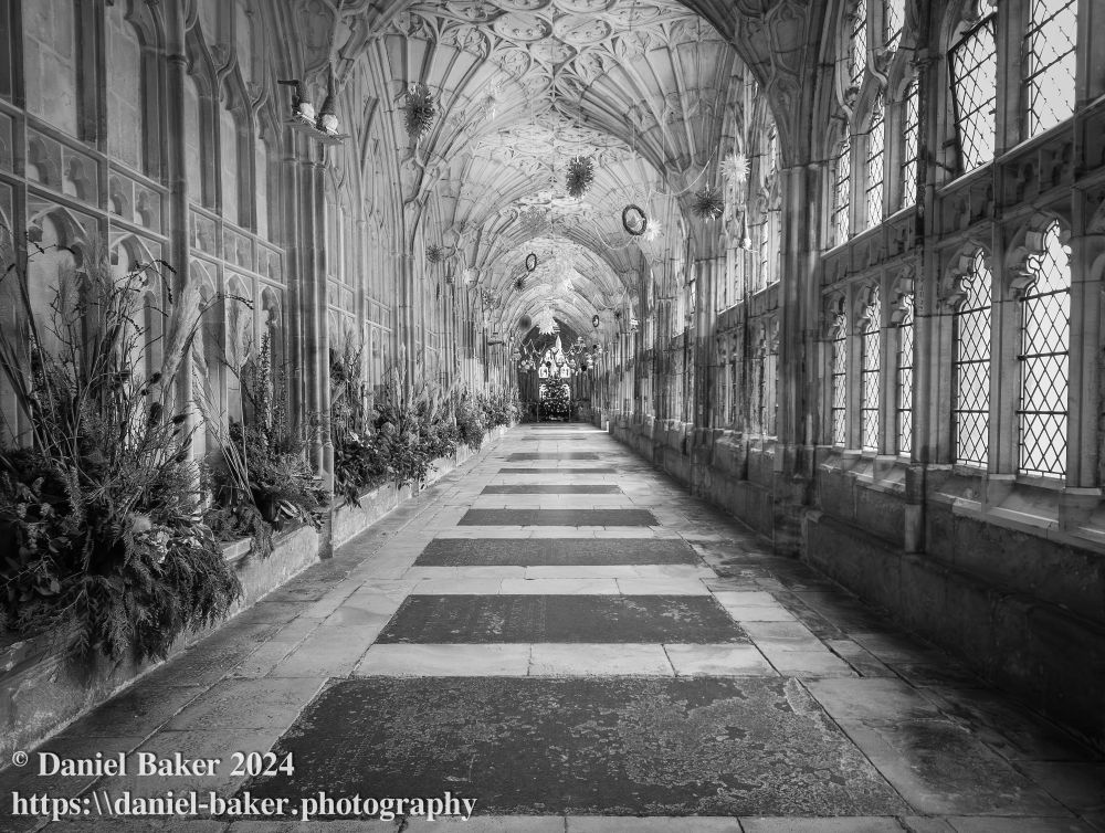 black and white photo of the cloisters at Gloucester cathedral with Christmas decorations hanging from the ceiling 