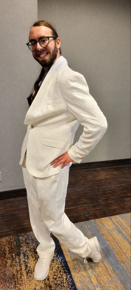 A man posing gayly in a white suit.