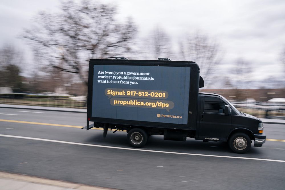 A black mobile billboard truck drives along a D.C. street. The background is blurred, making the truck the only object in focus. On the side of the truck, a LED screen reads: Are (were) you a government worker? ProPublica journalists want to hear from you. Signal: 917-512-0201. propublica.org/tips.