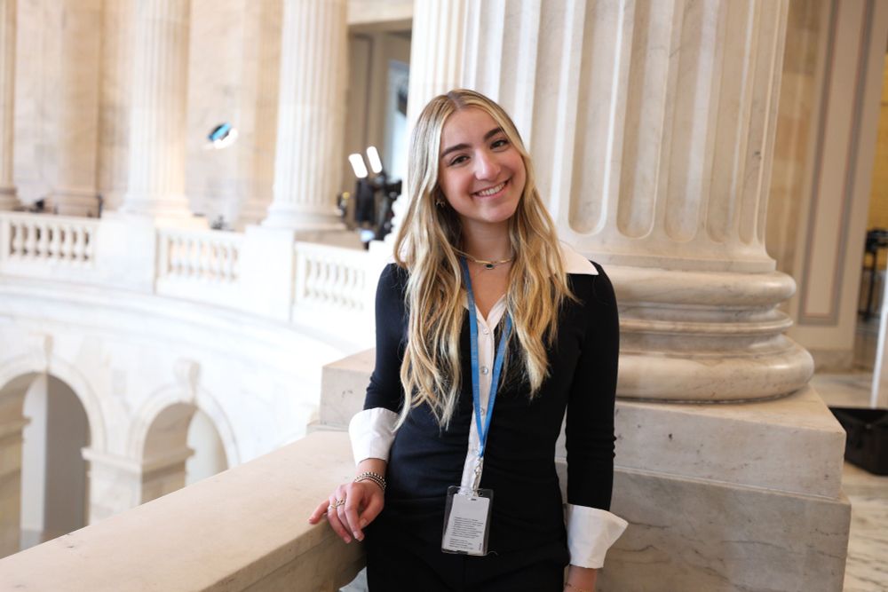 Zoe Singer, a sophomore at the Medill School of Journalism, poses against white marble columns. She wears a black and white blouse and a blue lanyard with a tag.