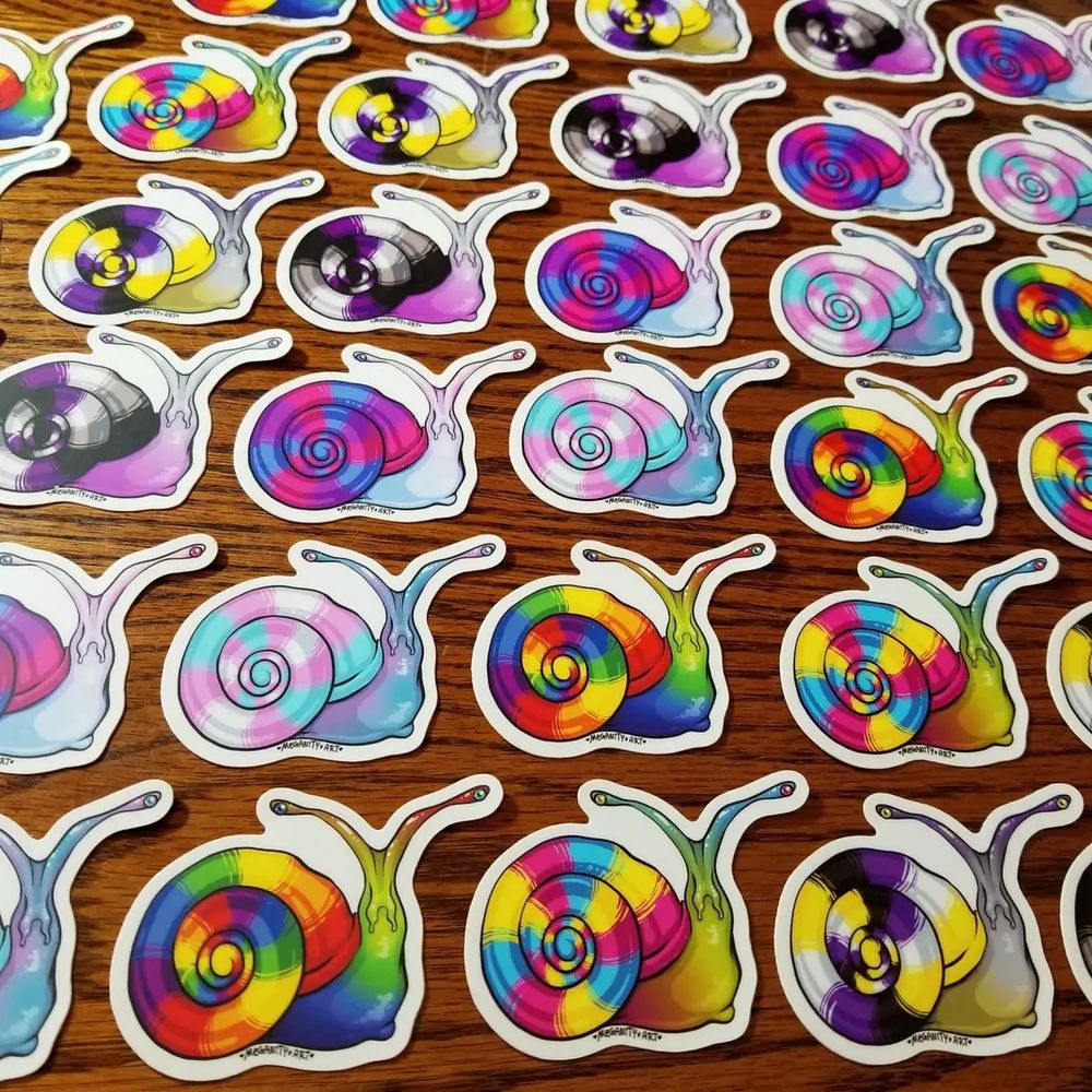 Pride Snail stickers arranged in a grid with each type arranged on the diagonal. Pride snails have long floppy antennae and a round, striped shell. Their shells have a pride flag in the stripes. Their bodies are soft gradients of the pride flags colors. Depicted are a number of pride flags: 6 color rainbow, pan, nonbinary, ace/demi, bi, and trans. They are waterproof stickers available on my etsy! 
Designed by Meganity Art!
