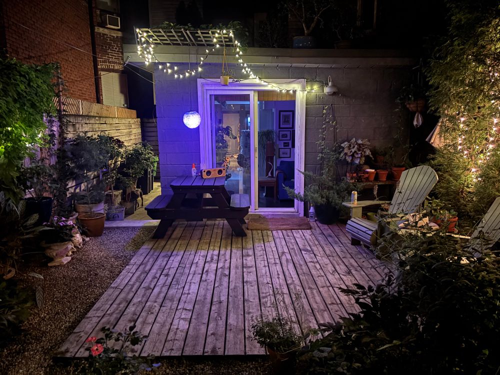 A photo facing the back of the house. There are faerie lights, a wooden deck and an open sliding glass door.