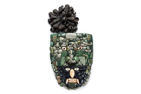 Máscara verde formada por un mosaico de piedras. En la zona de la boca, hay otra cara negra con grandes colmillos.