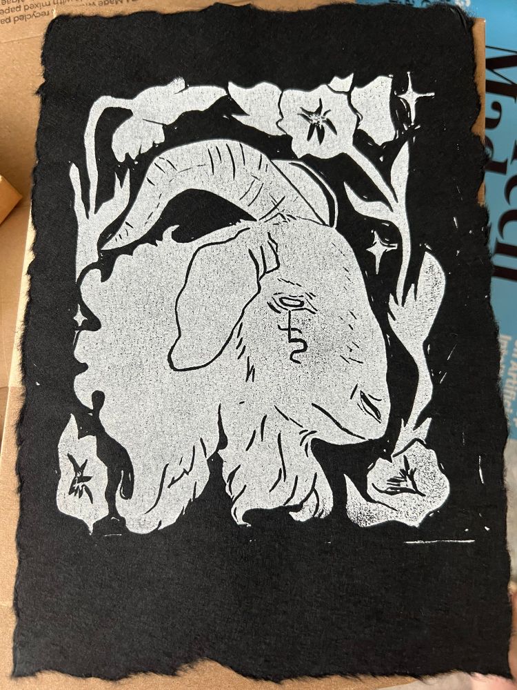 A photo of a linocut print of a white goat’s head on black mulberry paper