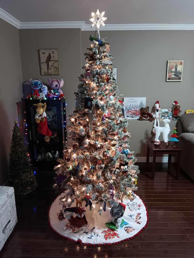 A artificial, white Christmas tree decorated with ornaments with a white tree skirt in a living room.