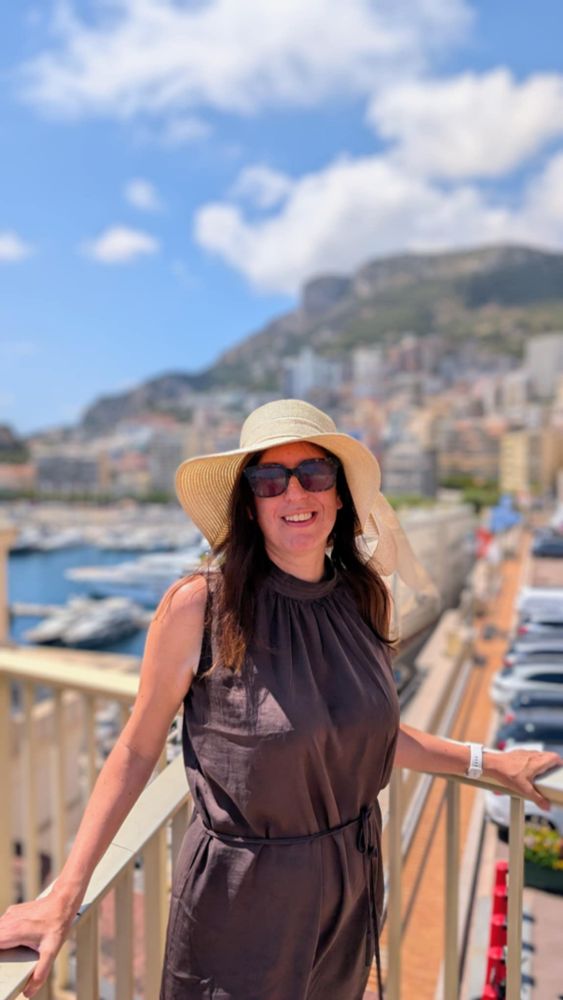 Monte-Carlo. Båtar i bakgrunden. Brun klänning.  Stor hatt och solglasögon. 