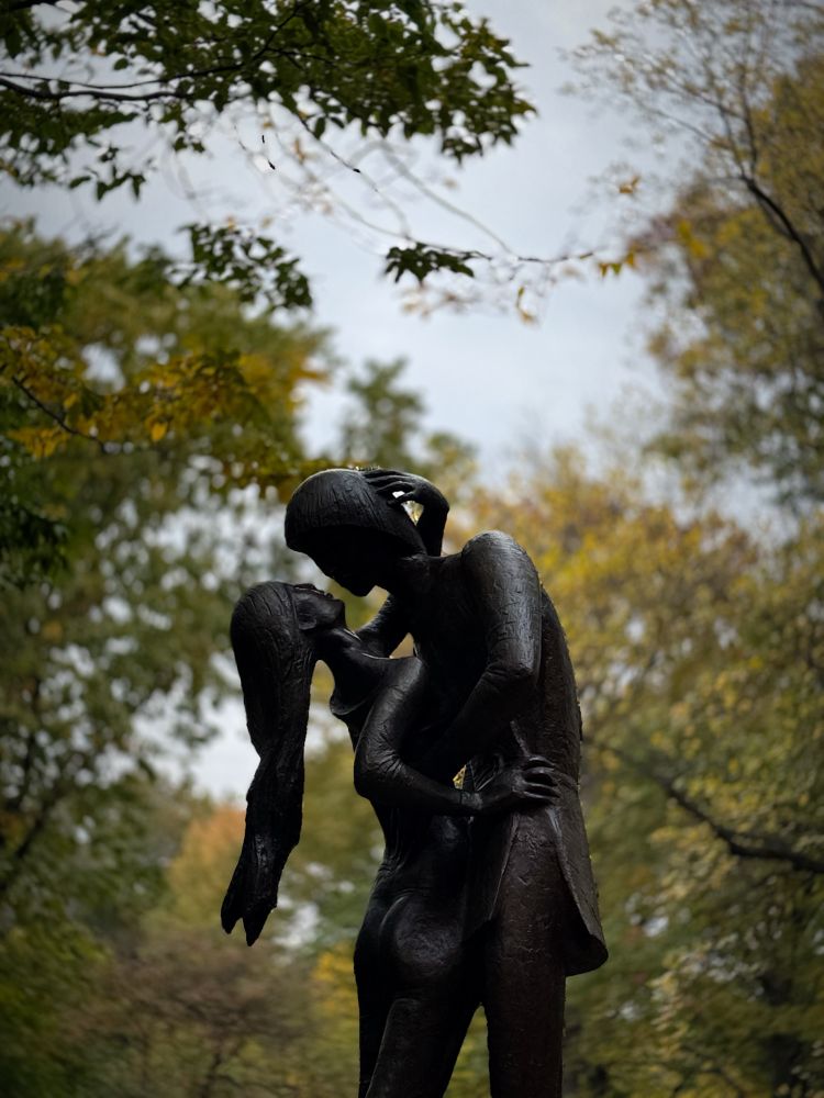 Statue of Romeo and Juliet with fall touched leaves on trees behind them. 