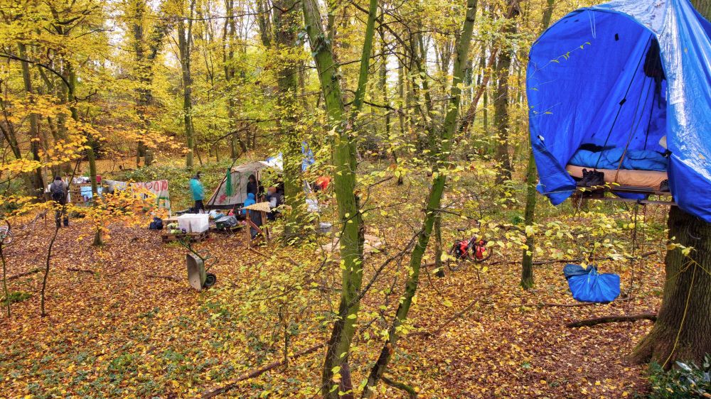 Hinten im Hintergrund das Küchenzelt, vorne eine erhöhte Struktur, die mit einer großen blauen Plane überdacht ist. 