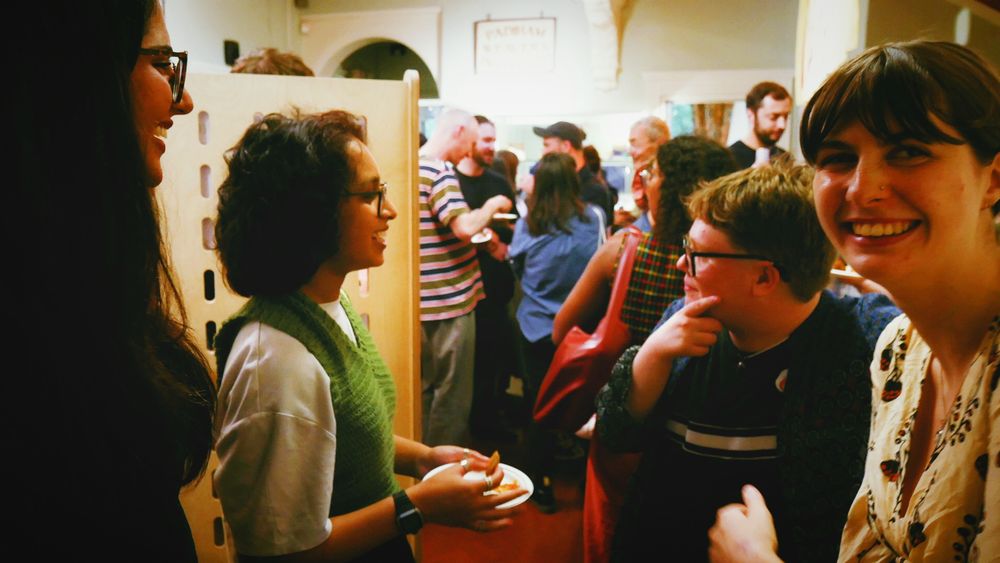Some of the Little Flames group chat to friends, smiling. A crowd of exhibition goers are seen in the background.