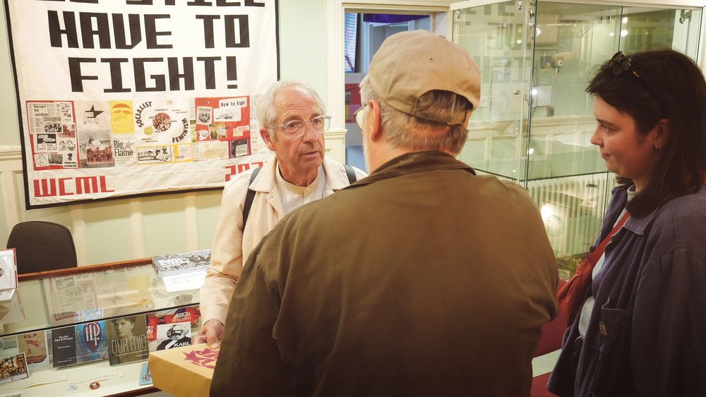 Two men and a woman chat to each other in front of the banner.