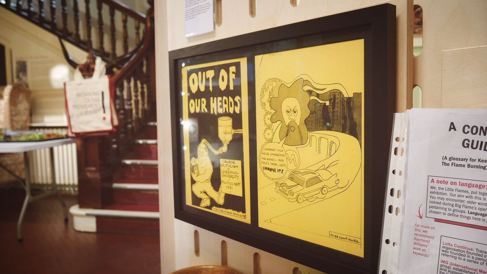 A framed archival cover spread of ‘Out of Our Heads’, a student pamphlet. It features a comical drawing of Marx on the back.