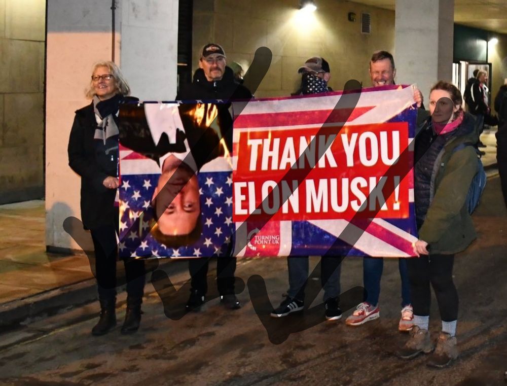 A watermarked image of 5 white people holding a banner in a car park. The banner says, "Thank you Elon Musk!" Edited to have an image of Elon flipped upside down. The text is on a Union Flag with stars in the corner.
