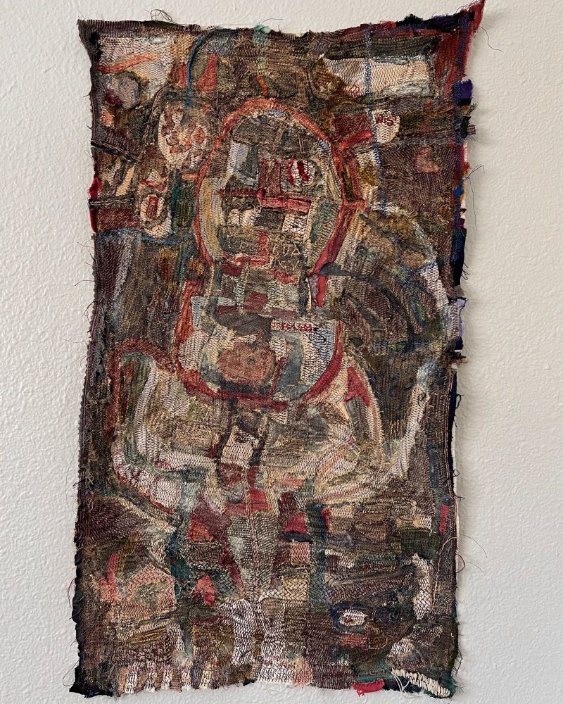 A small tapestry made of many small scraps of fabric sewn tightly together, hung on a wall 