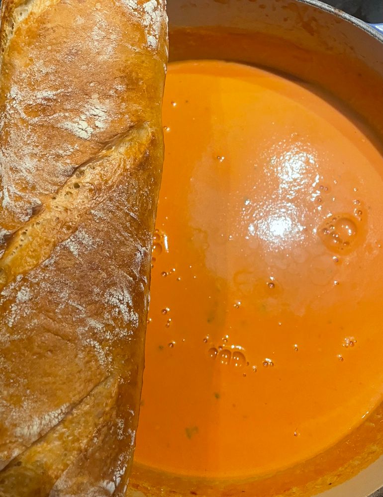 A pot of tomato soup with a fresh baguette sitting atop it. 