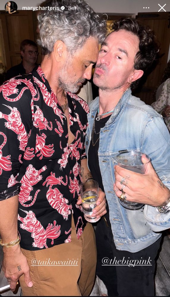 Taika in a shirt with pink tigers on it, smoking an drinking water or something clear with Robbie Furze who is in the band the big pink and one of Rita’s close friend Mary’s husband. Taika has his eyes closed and is resting his forehead on Robbie’s cheek.
